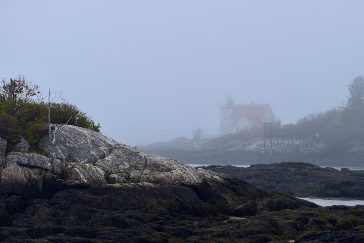 Fog over a rocky Atlantic shore with a lighthouse house in the distance